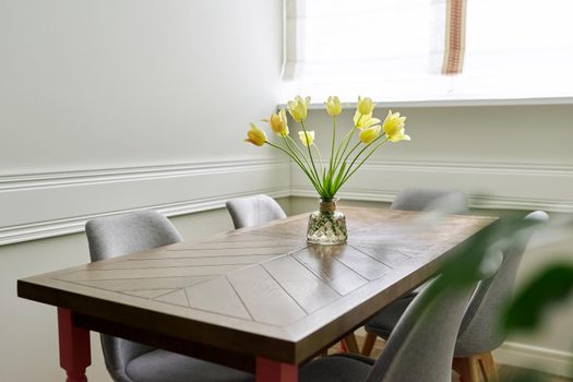 Vase with a bouquet of yellow tulips on a wooden table in the interior of the living room