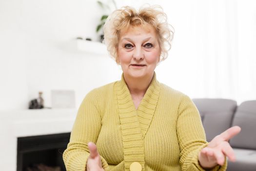 Smiling middle aged mature grey haired woman looking at camera, happy old lady posing at home indoor, positive single senior retired female sitting on sofa in living room headshot portrait