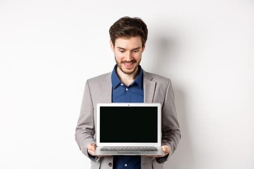 Handsome caucasian businessman in suit showing empty laptop screen, demonstrate promo, standing on white background.