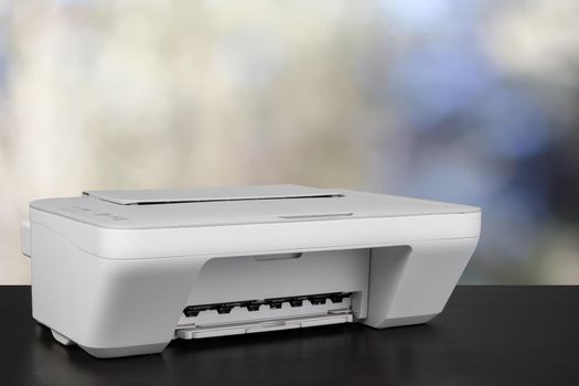 Compact laser printer on black desk against blurred background, close up