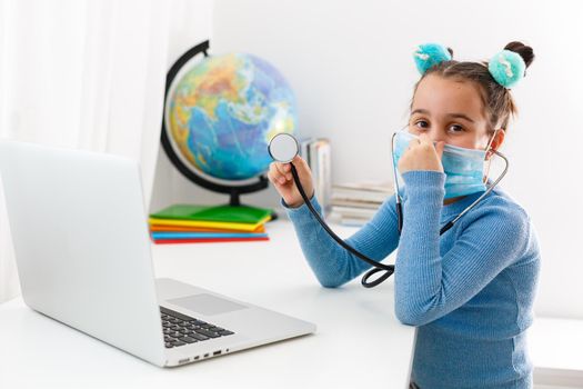 Learning about all sorts of stuff on the web. Little girl uses the mask as a pandemic protection. Using laptop.