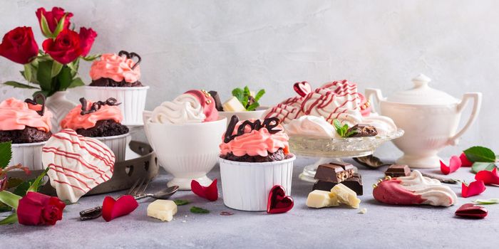 Beautiful chocolate cupcake, pink cream, meringue cookies and red roses on gray stone background. Valentines, Mother Day, wedding concept with with copy space. Banner.