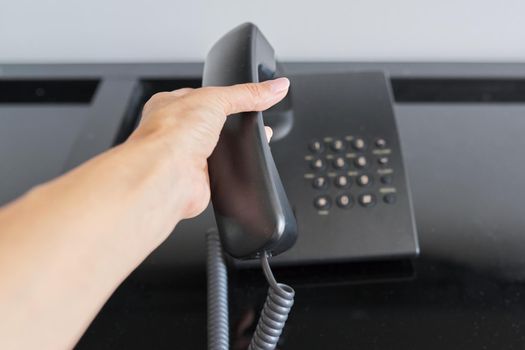 Telephone in a hotel room, hand with a raised telephone receiver close-up. Service, help, maintenance, communication with the administration reception