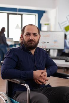 Portrait of smiling disabled businessman working at marketing strategy in startup company office. Paralyzed executive manager analyzing financial graphs planning business partnership