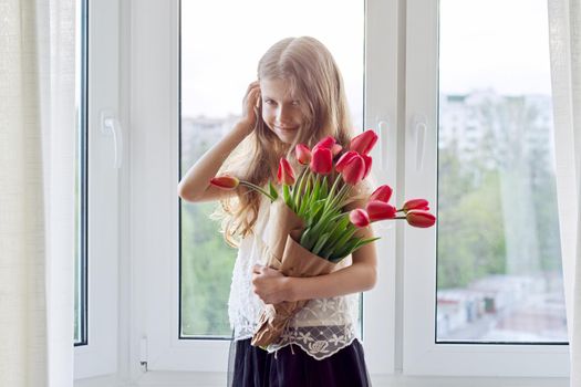 Mother's day, girl child with bouquet of red tulips flowers at home near the window. Gift for mom, love, congratulations, mom's holiday concept