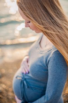 Pregnant young woman standing on the beach in a gray knitted dress, sunset, Pregnancy concept