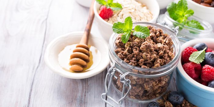 Homemade chocolate granola ingredients, nuts, oats, honey and berries on white wooden background. Healthy breakfast concept with copy space.