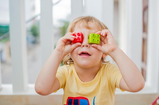The boy makes eyes of colorful children's blocks. Childhood concept. Cute little kid boy with glasses playing with lots of colorful plastic blocks indoor. Active child having fun with building and creating of tower. Promotion of skills and creativity