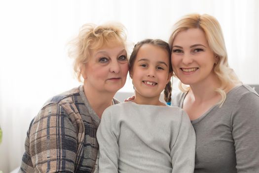 Three generations of women. Beautiful woman and teenage girl are kissing their granny while sitting on couch at home