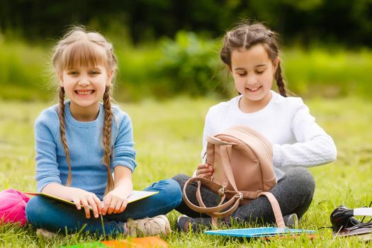 two pretty schoolgirls sit with books outdoors in the park. Schoolgirls or students are taught lessons in nature.