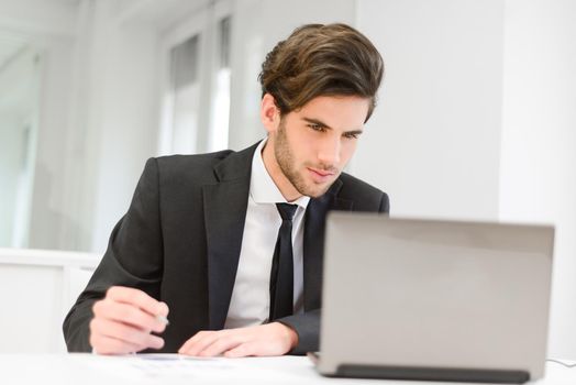 Portrait of a smiling businessman sitting at his laptop and working in his office