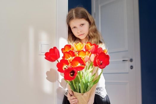 Mother's day, girl child with bouquet of red tulips flowers at home near the door. Gift for mom, love, congratulations, mom's holiday concept