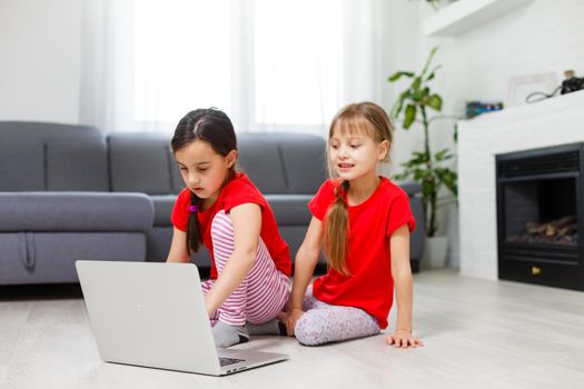 Two little girls sitting in front of a laptop and laughing, close-up, positive emotions, entertainment on the Internet for children