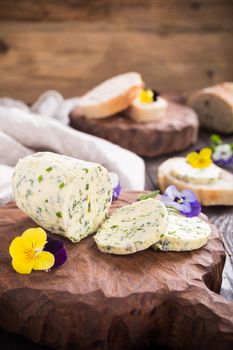 Herb butter with edible flowers on wooden cutting board, healthy food.