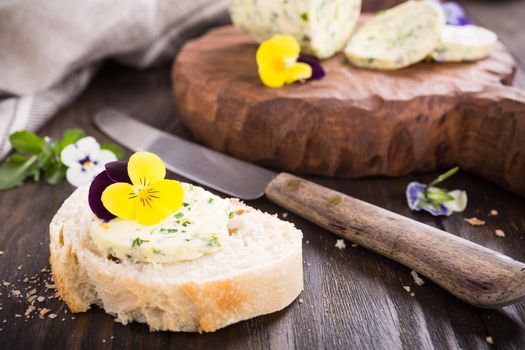 Sandwich with herb and edible flowers butter on wooden background, healthy food.