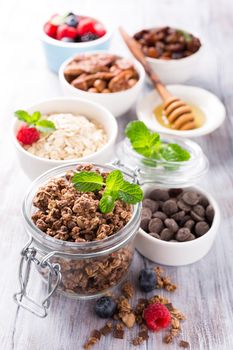 Homemade chocolate granola ingredients, nuts, oats, honey and berries on white wooden background. Healthy breakfast concept.