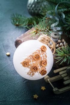 White Christmas ball decorated with christmas tree and decoration on old black stone background. Winter holiday concept. Retro style toned.