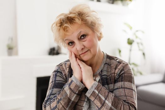 Smiling middle aged mature grey haired woman looking at camera, happy old lady posing at home indoor, positive single senior retired female sitting on sofa in living room headshot portrait