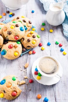 Homemade cookies with colorful chocolate candies with cup coffee on old white wooden table.