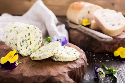 Herb butter with edible flowers on wooden cutting board, healthy food.