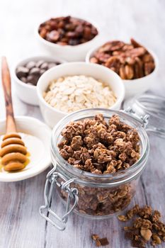 Homemade chocolate granola ingredients, nuts, oats, honey on white wooden background. Healthy breakfast concept.