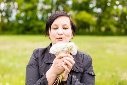Girl blowing on white dandelion in the forest
