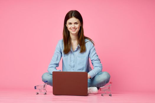 woman sitting on floor with laptop shopping entertainment pink background. High quality photo