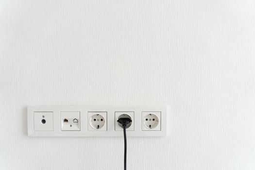 black cable cord pluged in receptacle of modern electric socket in multi paneling, internet, tv or radio adapter socket on white wall background at hom