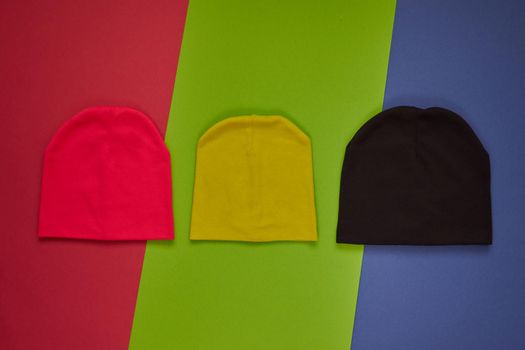 Colorful vivid kids hats. Demi season autumn children's fashion wear. Top view on pink green blue background.