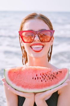 cheerful woman in sunglasses eating watermelon by the ocean. High quality photo