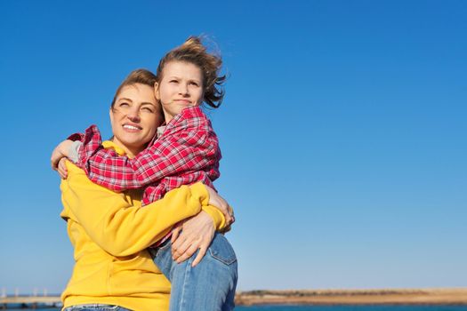 Outdoor portrait of happy smiling mom and child daughter hugging together, blue sky background space for copy space, family, love, happiness, joy, childhood concept