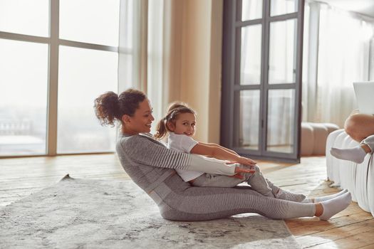 Happy woman is cuddling with her daughter while doing balance workout together in living room