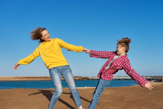 Happy mom and daughter child have fun together on the sea beach. Blue sky background, family, love, happiness, joy, childhood concept