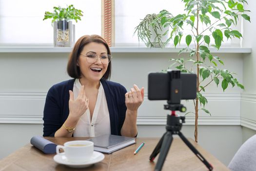 Video blog vlog stream, woman looking at smartphone webcam on tripod, recording video, talking online, sitting at table at home. Educational channel, journalist, columnist, psychologist, assistant