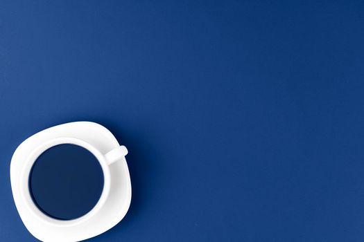 Top view of a cup of coffee on saucer on classic blue background. Close up.