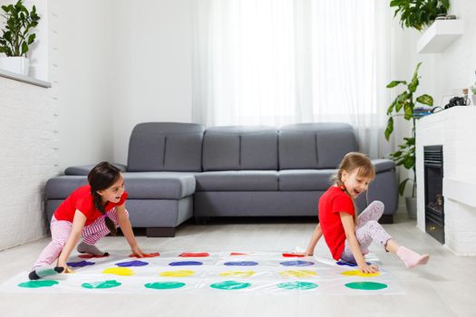 Two happy girls in children's clothes enthusiastically play on the floor.