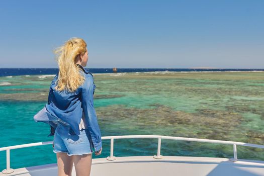 Young blonde female on yacht looking at turquoise coral reefs in Red Sea. Tourism, nature, travel, diving, snorkeling, water world concept, copy space