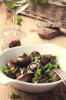 Baked champignons mushrooms with butter, parsley and roasted garlic in white bowl. Selective focus. Healthy food concept. Toned photo.