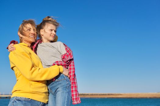 Outdoor portrait of happy smiling mom and child daughter hugging together, blue sky background space for copy space, family, love, happiness, joy, childhood concept