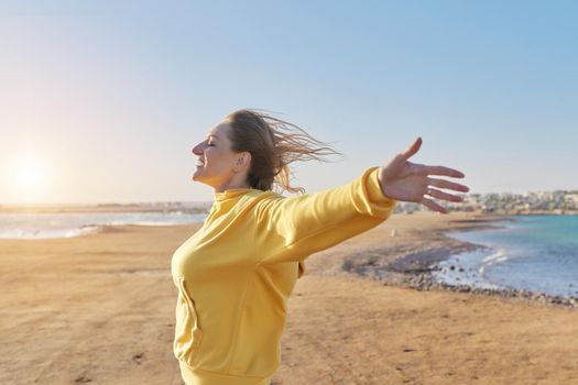 Beautiful happy mature woman with open arms closed eyes enjoying the sunset on the seashore. Freedom, joy, happiness, nature, vacation, middle-aged people concept