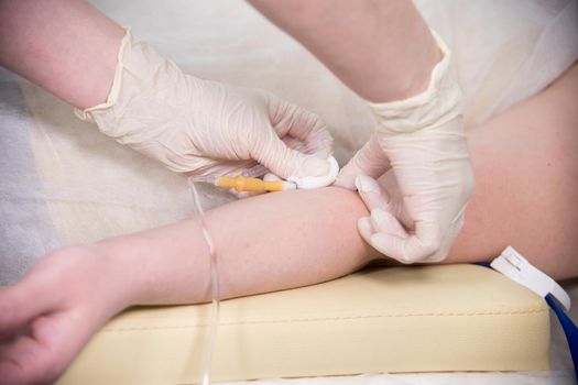 A nurse in gloves taking a blood sample from a hand for testing. Mid shot
