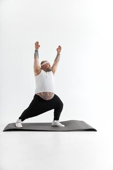 Sporty fat man with beard and tattoos is doing yoga