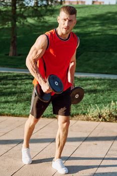 athletic man with dumbbells in his hands outdoors in the park. High quality photo