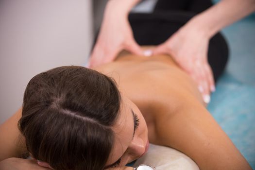 Masseur doing a back massage to a young slim woman with tanned skin with closed eyes at the clinic, her head and shoulder in the front view