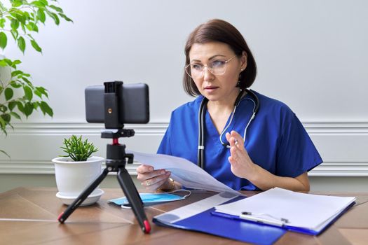 Online doctor consultation, female specialist talking with patient using video call, smartphone on tripod, doctor with stethoscope looking at the phone's webcam