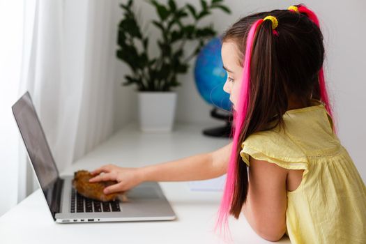 Cheerful young little girl with a pet hamster using laptop computer studying through online e-learning system at home. Distance or remote learning