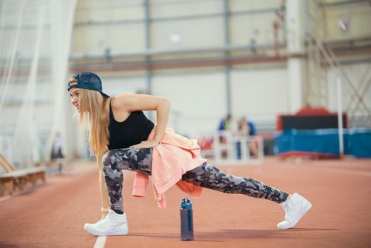 Young athletic woman doing exercise lunge in sports arena. Mid shot
