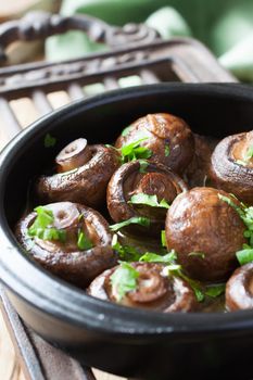 Baked champignons mushrooms with butter, parsley and roasted garlic in black bowl. Selective focus. Healthy food concept.