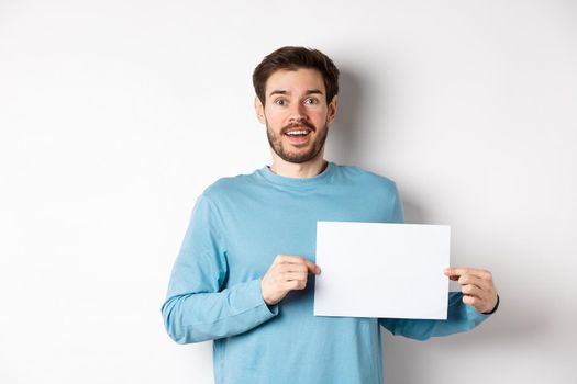 Romantic man looking with hopeful face at camera, showing sign card, blank piece of paper for banner or logo, standing over white background.