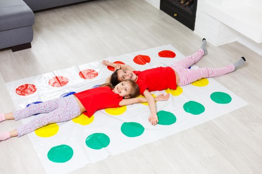 Two happy girls in children's clothes enthusiastically play on the floor.